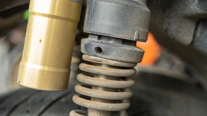 A detailed close-up of a motorcycle shock absorber showing wear and tear, with dusty coil springs....