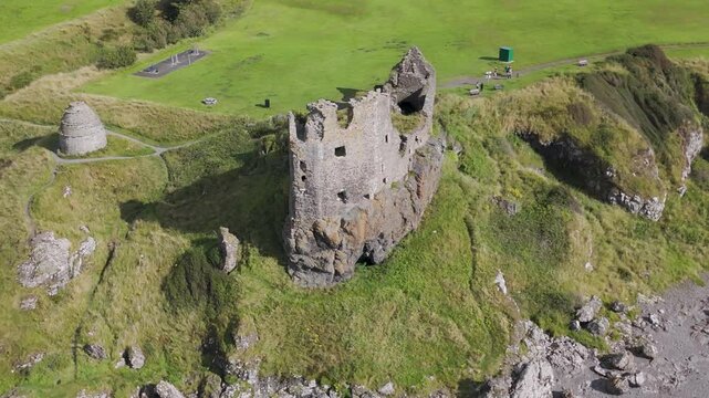 Camera panning around dunure castle ruins on green cliff