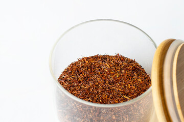 rooibos tea in a glass opened jar with wooden cap isolated on white background