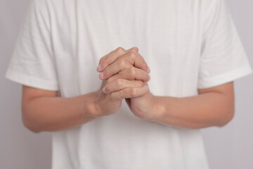 A man wearing a white shirt with both hands clasped together in a gesture to pray to God. hand shape for good wishes.