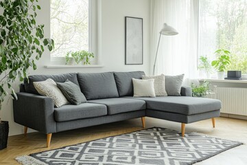 Fototapeta premium A stylish living room showcasing a dark gray corner sofa accented with pillows, surrounded by fresh greenery, and a large window, complemented by a geometric gray and white rug.