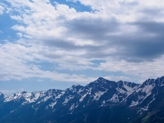 Fototapeta premium An amazing fusion of nature: green meadows at the foot of the mountains, soft clouds framing the peaks, creating a harmonious landscape