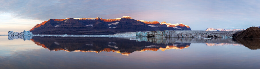 A panorama of Vikinge Bay, Scoresby Sund, Greenland, showing icebergs, mountains, a glacier, and...