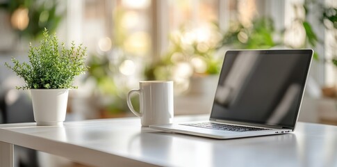 Fototapeta premium Minimalist white office desk with laptop and coffee mug on blurred background