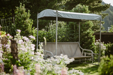 Naklejka premium a cozy garden corner with swing chair in a hotel, with flower in the foreground, Dolomites, Italy