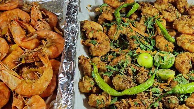 Background of fried crunchy peeled shrimps with parsley, fried green chili pepper and lemon, seasoned with salt, pepper, spices and grilled unpeeled shrimps with colored bell peppers slices and sauce