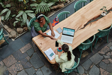 Top down view of two young businesswomen giving handshake to each other during meeting in cozy green cafe © AnnaStills