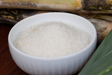 A perfect display of white sugar in a ceramic bowl, paired with a spoon and fresh cane leaves, capturing the essence of natural sweetness.
