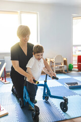 Physical therapist assists a young boy with movement disorders as he engages in physical...