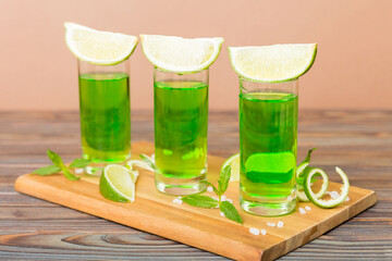 Sweet refreshing mint liqueur, with ice and mint leaves on table background, Shots with lime slice and mint flat lay