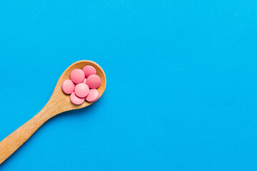 Vitamin capsules in a spoon on a colored background. Pills served as a healthy meal. Red soft gel vitamin supplement capsules on spoon