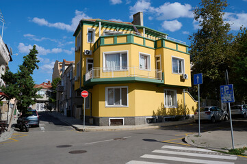Bright yellow architectural design in a corner setting with clear skies and parked cars on a sunny day, Varna, Bulgaria