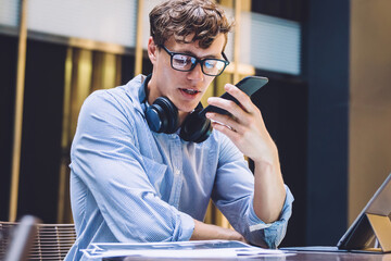 Serious male entrepreneur recording voice message during online communication with personal secretary solving problems while checking mistakes on financial report, concept of business people
