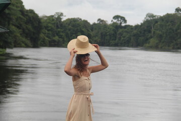 mulher com vestido claro e chapéu na beira de rio em hotel de selva em alta floresta, mato grosso 