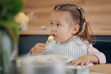 Little girl holds fork on her own and eats healthy breakfast from milk. Concept independent kid, eating super food