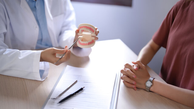 Asian dentist doctor women holding model of human jaws with teeth explaining about oral dental treatments to female patient while examination teeth and discussion about dental health in dental clinic