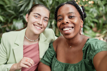 Selfie of two gorgeous and jolly biracial friends in green cafe