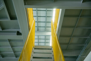 Industrial walkway with yellow handrail and steel structure roof inside the factory, equipped with a staircase secured by handrails.