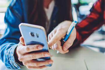 Cropped image of male and female students browsing social network via cellular phone during break from studying togetherness indoors, friends searching information on website via smartphone gadget