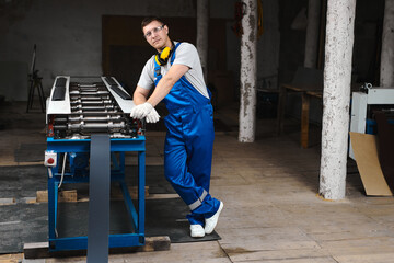 Professional engineer man in blue uniform works in factory. Rolled metal, metal processing and manufacturing of metal fence