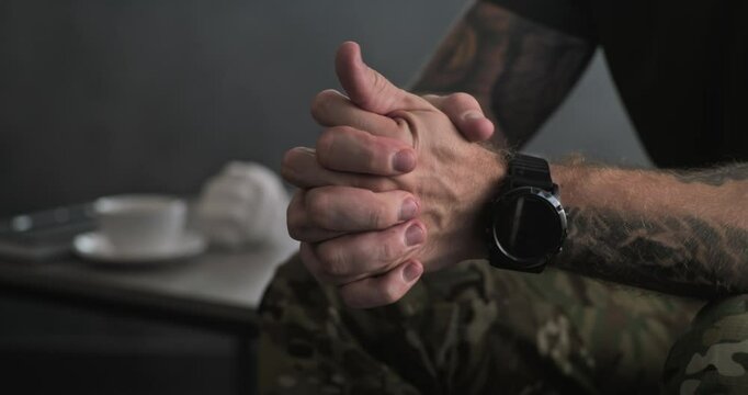 Close up of nervous military man in uniform sitting and clenching hands during therapy session with psychotherapist. Soldier with contusion or PTSD on rehabilitation. Post traumatic stress disorder.