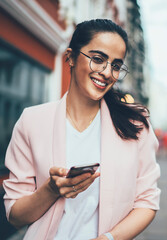 Half length portrait of cheerful Spanish woman in spectacles for provide eyes protection laughing at camera while waiting for text comments from followers after publicate article in social network