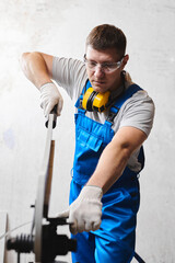 Professional engineer man in blue uniform works in factory. Rolled metal, metal processing and manufacturing of metal fence