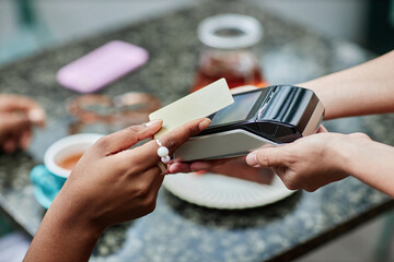 Unrecognizable female hand tapping her credit card while hand of waitress holding terminal