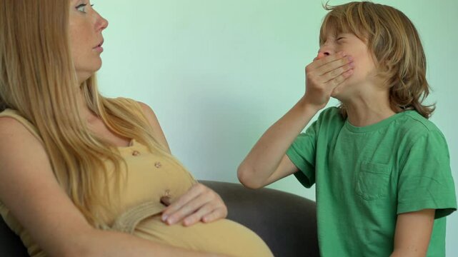 A pregnant woman and her elder son sit on a couch. Suddenly, he sneezes, and she reacts with concern, highlighting the potential dangers for her unborn child. This video captures the protective