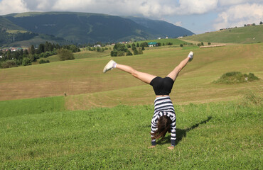 agile athletic girl performs a perfect cartwheel with her legs high up in the air on the mountain...