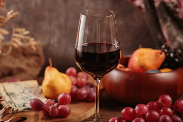 Glass of red wine served with blue cheese on dark wooden background. Autumn picnic with wine and cheese platter, fruits and dry leaves in rustic style