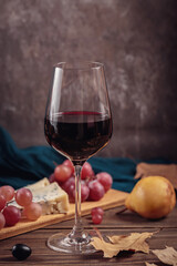 Glass of red wine served with blue cheese on dark wooden background. Autumn picnic with wine and cheese platter, fruits and dry leaves in rustic style