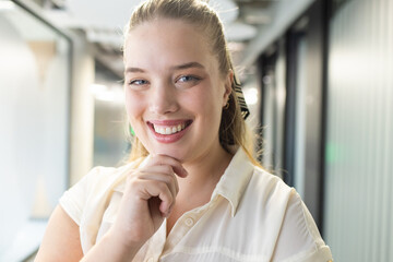 Fototapeta premium Smiling businesswoman in office hallway, wearing white blouse and looking confident