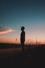 Fototapeta premium A silhouetted person standing in a field at sunset, evoking a sense of peaceful contemplation and tranquility.