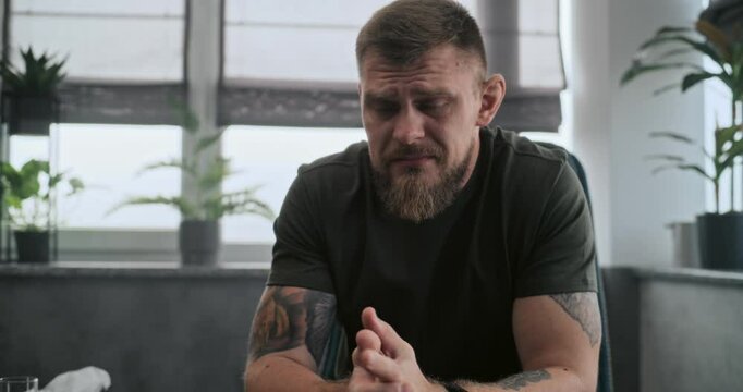 Scared and upset military man with PTSD sits in chair, cries and remembers his traumatic experience during psychotherapy session with therapist or psychologist. Psychological assistance. Slow Motion.