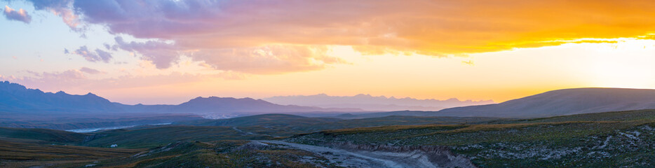 The picturesque sunset colors the mountain landscape with bright orange shades, creating a spectacular view over the peaks of the mountains. winding mountain winding road is visible in the foreground