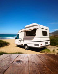Table background with a wooden board and sunny beach and ocean and a camper van
