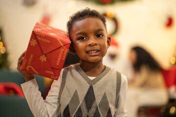 A young child excitedly holding a Christmas gift box, surrounded by festive decorations and...