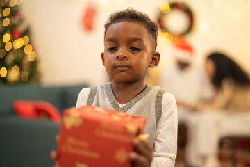 A young child excitedly holding a Christmas gift box, surrounded by festive decorations and...