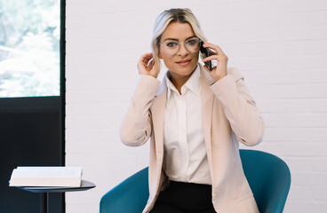 Portrait of attractive caucasian female entrepreneur in stylish spectacles for vision correction using smartphone application for making business call, executive manager talking with colleague