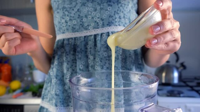Woman pouring condensed milk in blender preparing Brazilian lemonade on kitchen. Recipe cuisine culinary cooking. Prepare citrus fruit dessert homemade fresh beverage.