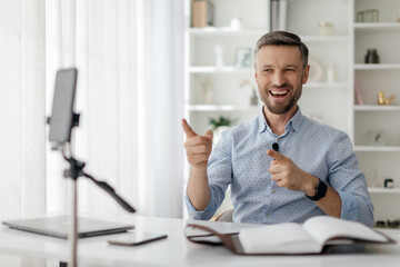 A smiling man gestures enthusiastically during a virtual discussion at his well-organized desk,...