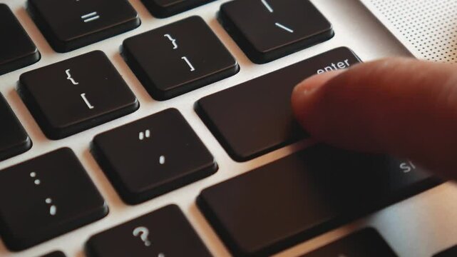 Closeup of finger pressing enter key on modern laptop keyboard. Man pushes enter button on notebook. 