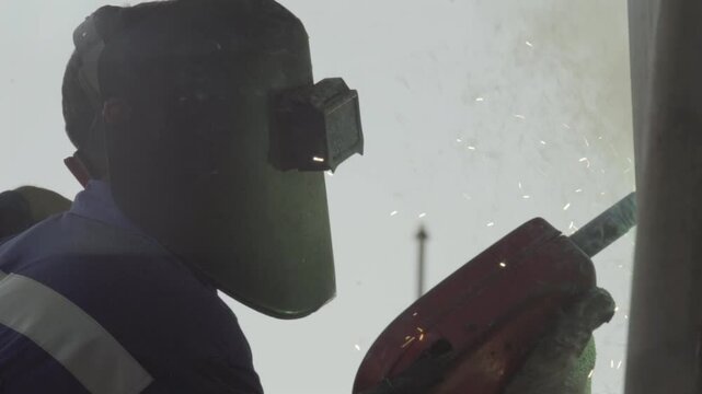A welder with all necessary safety equipment, welding metal parts of a boat