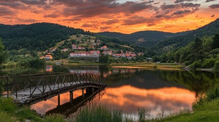 Serene sunset over a tranquil lake with a wooden bridge and a picturesque village backdrop.