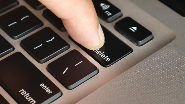 Finger of the computer user, he presses the delete button on the computer keyboard.