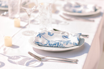 An elegant table set up with white plats, silverware, candles, and a blue and white napkin on a...