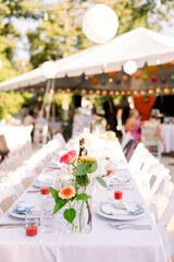 A backyard set up for a wedding reception with a tent in the background, and the table is set up with white tablecloths, flowers, and porcelain plates. 