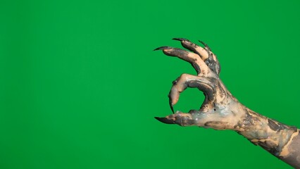 Creepy halloween monster hand in black paint with nails shows ok good gesture sign, isolated on chroma key green screen background, workspace mockup.