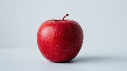 A single, perfectly ripe apple, its vibrant red skin contrasting against the crisp white background